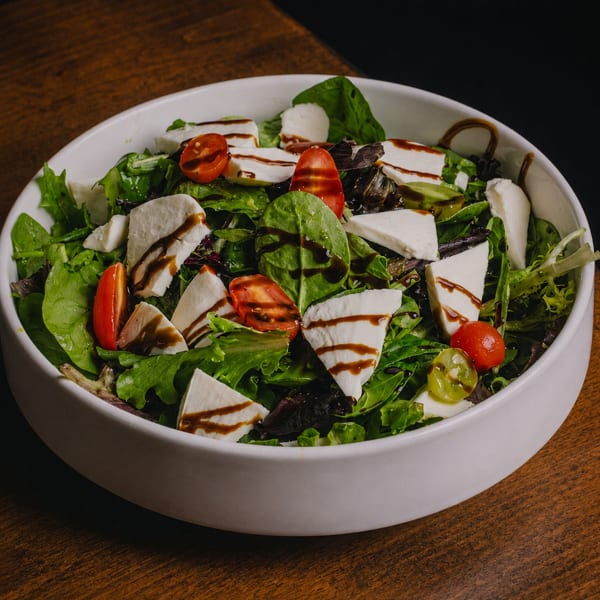 Fresh garden salad with mozzarella, cherry tomatoes, and balsamic glaze in a white bowl.